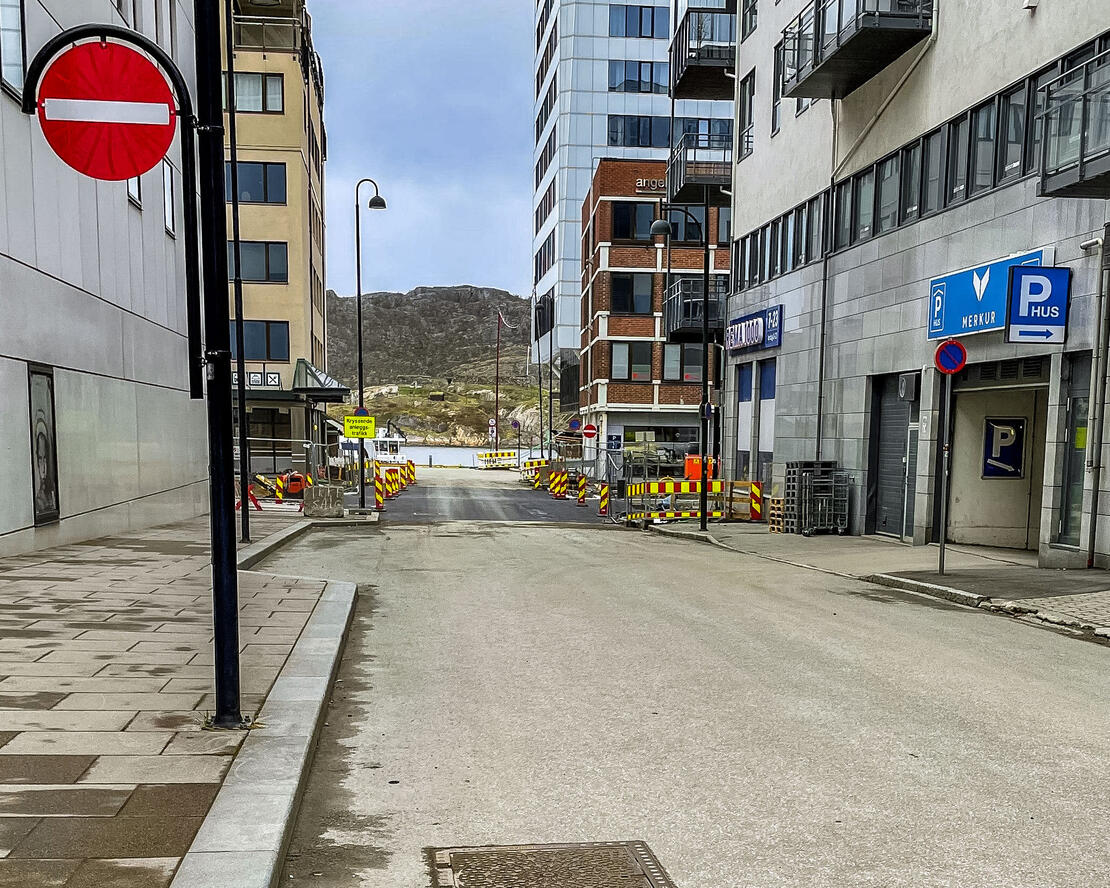 Bildet er tatt fra Sandgata, ovenfor innkjøringen til torvgarasjen, mot krysset til Sjøgata. Krysset er nylig asfaltert, med varselskilt på begge sider. 