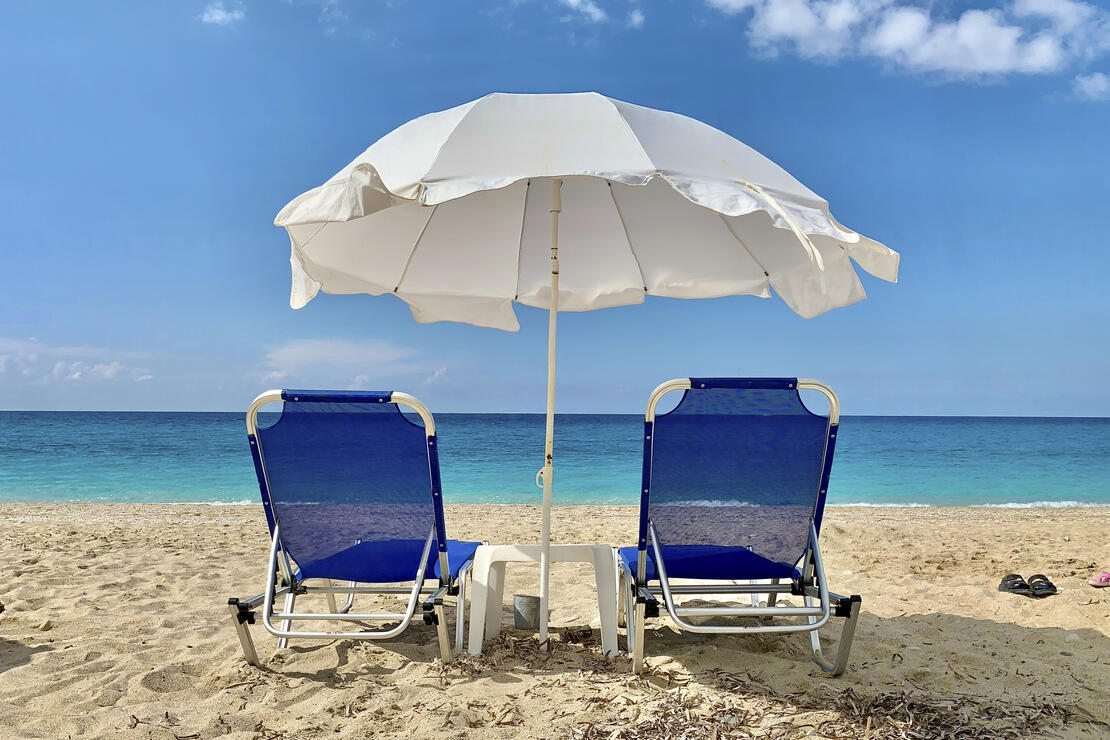 Bildet viser to solsenger og en parasoll på stranden med havet foran og blå himmel. 