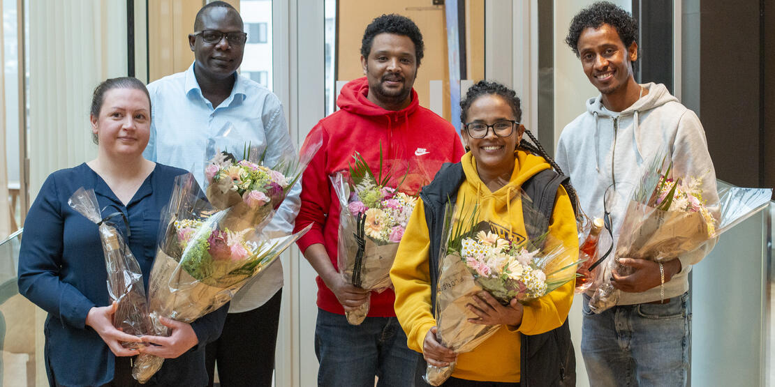 Bildet viser Bana Alsaad, Ashweil Alor, Amanuel Tedla, Semhar Gebreslasie og Mulue Sbhatu som står med hver sin blomsterbukett i forbindelse med feiringen av at de har fått fagbrev som helsefagarbeidere. Bildet er tatt inne på rådhuset i Bodø. 