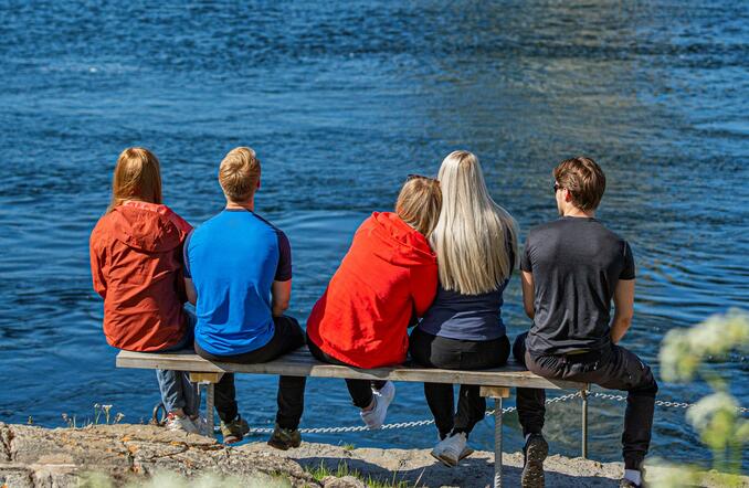 På bildet sitter fem ungdommer på en benk, med ryggen vendt mot kamera. Benken er plassert med utsikt over Saltfjorden og deler av Saltstraumen. 