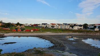 Bildet viser det aktuelle området i Breivika. Fjære, strand, hav, rorbuer, hus, gressplener, himmel. 