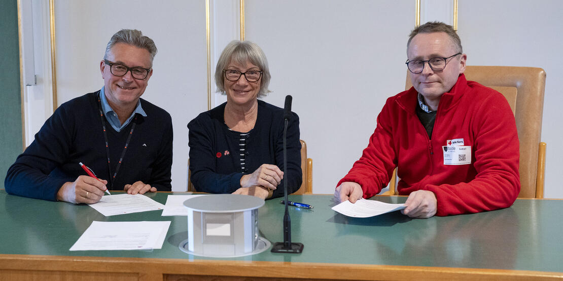 Tre personer som sitter ved et bord og signerer avtaler med penn og papir. 
