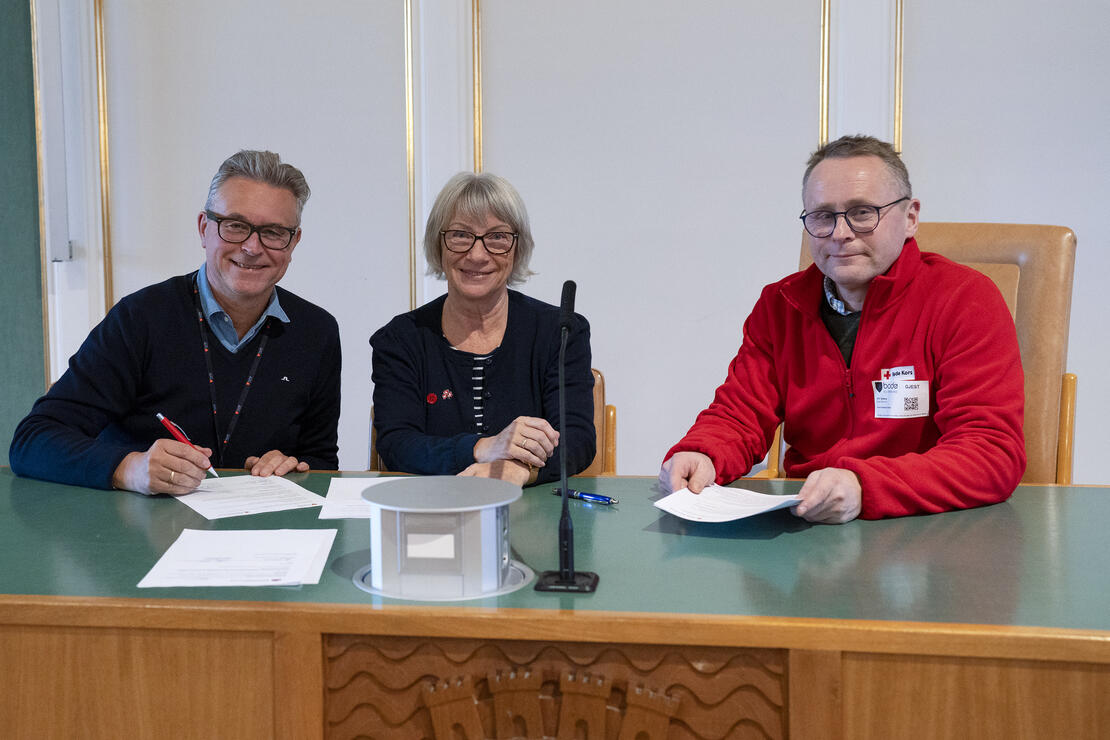 Tre personer som sitter ved et bord og signerer avtaler med penn og papir. 