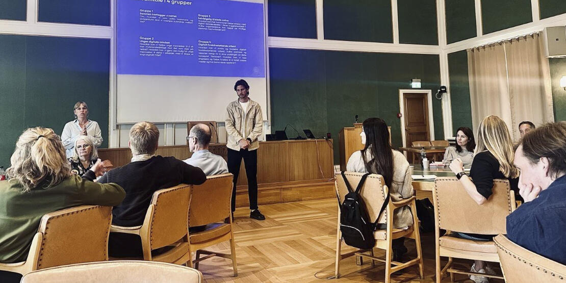 Bildet viser flere personer i bystyresalen i Bodø rådhus. To av personene på bildet holder en presentasjon. 
