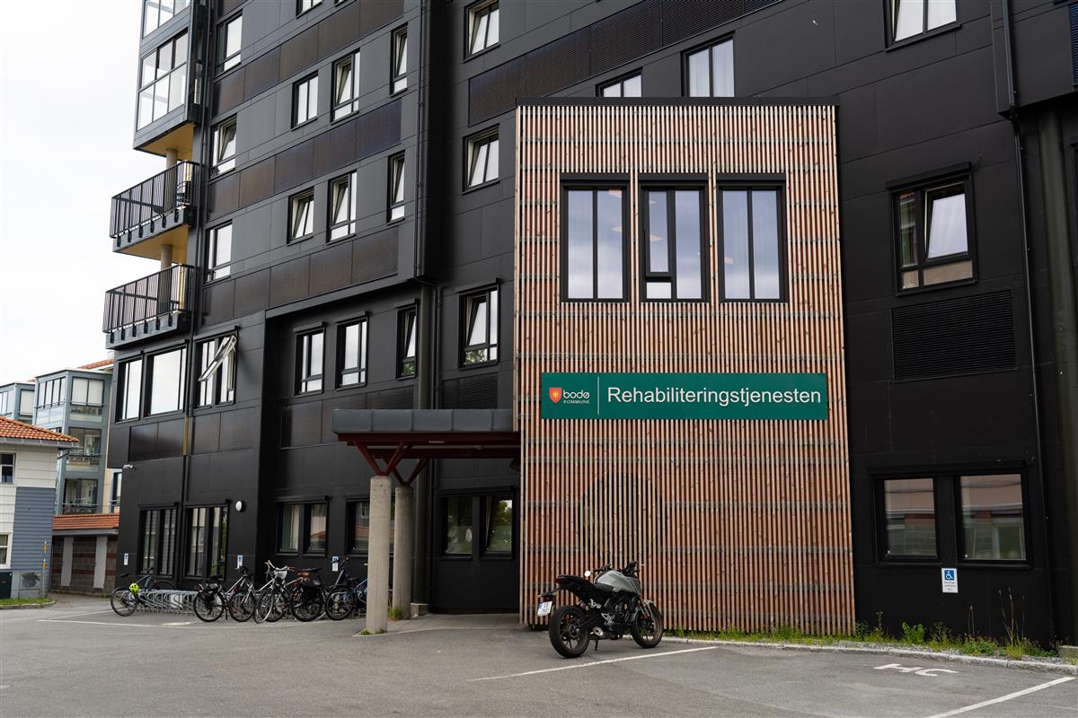 Inngangen til et mørk bygg. Deler av inngangen er i spiler og har et grønnt skilt på hvor det står rehabiliteringstjenesten på. Foto: Preben Hunstad - Klikk for stort bilde