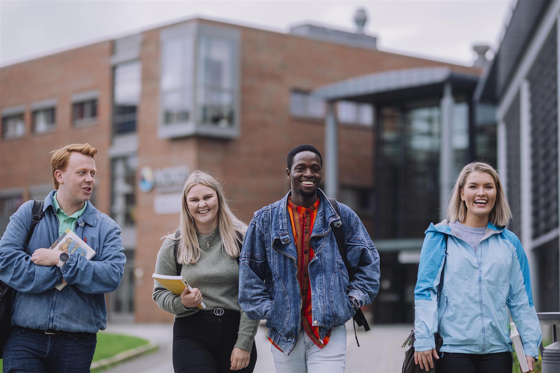 Fire blide studenter går utenfor universitetsbygningen.