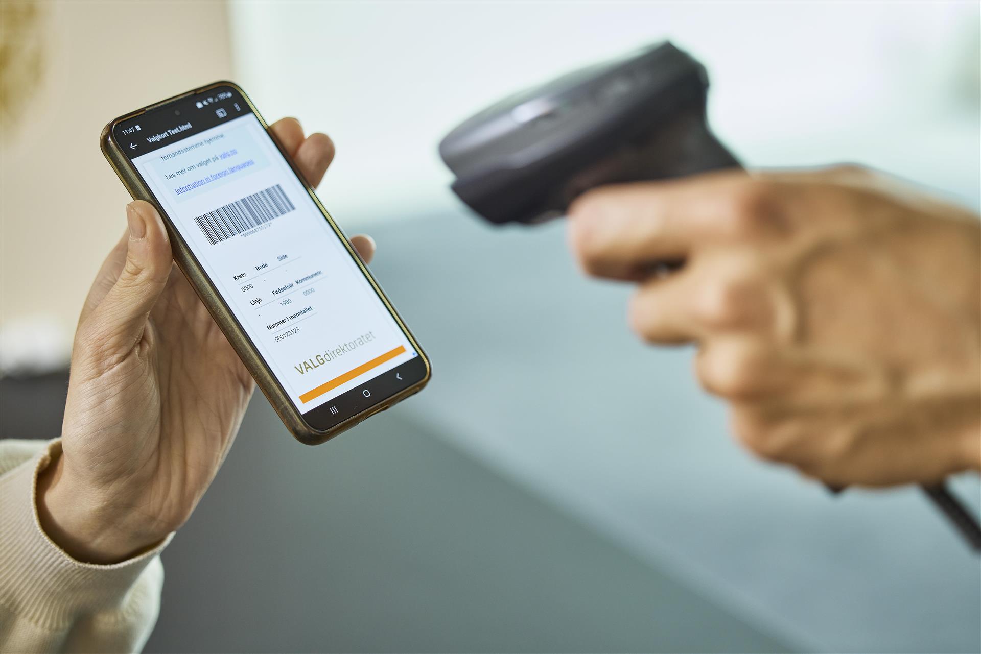 Bilde av noen som scanner en strekkode på en mobiltelefon, i forbindelse med valg. 