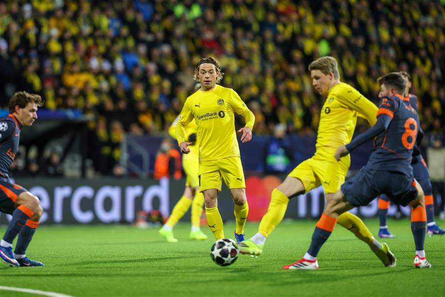 Glimt-spiller Jens Petter Hauge skyter fotballen, mens spillere fra Inter Milan forsøker å blokkere. Glimt-spiller Patrik Berg og publikum i bakgrunnen.